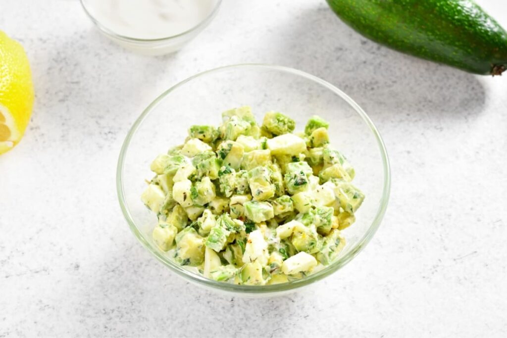 Bol din sticla cu salata de oua cu avocado si iaurt pe masa alba