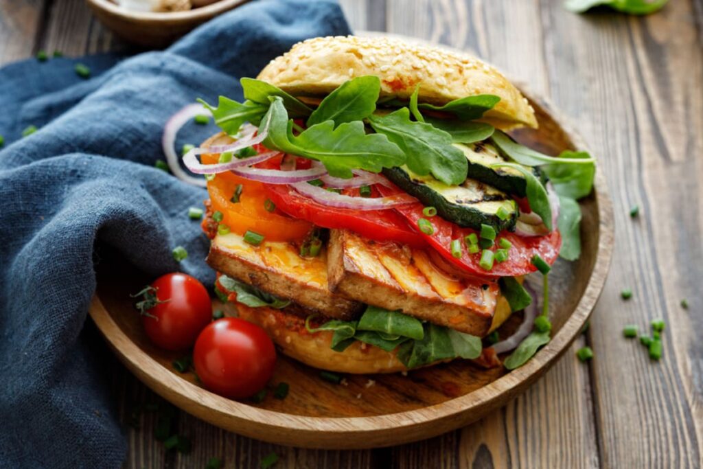Burger vegetarian cu tofu, rosii, ceapa si salata pe farfurie din lemn