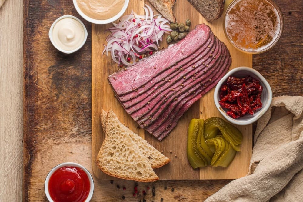 Felii de pastrama de oaie pe tocator cu ceapa, muraturi, paine si sosuri