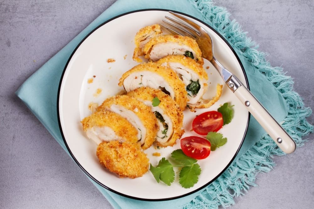 Piept de pui Kiev taiat pe farfurie cu rosii si patrunjel