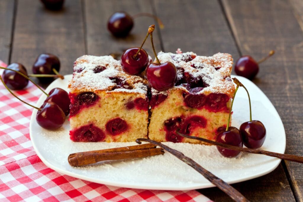 Bucati de prajitura cu cirese si iaurt pe farfurie langa cirese