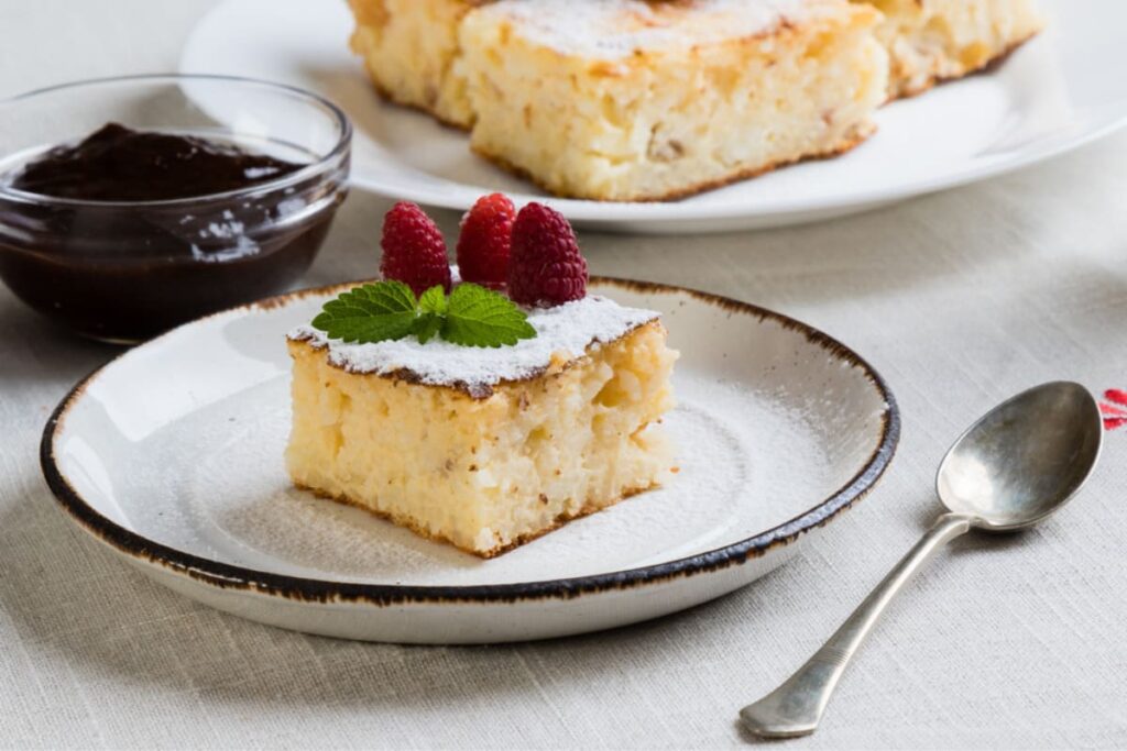 Budinca de orez cu lapte decorata cu zmeura, menta si zahar pudra pe farfurie