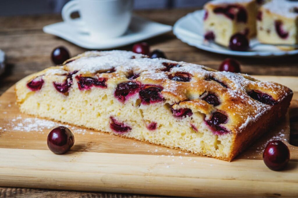 Prajitura cu cirese si iaurt servita cu zahar pudra pe tocator din lemn