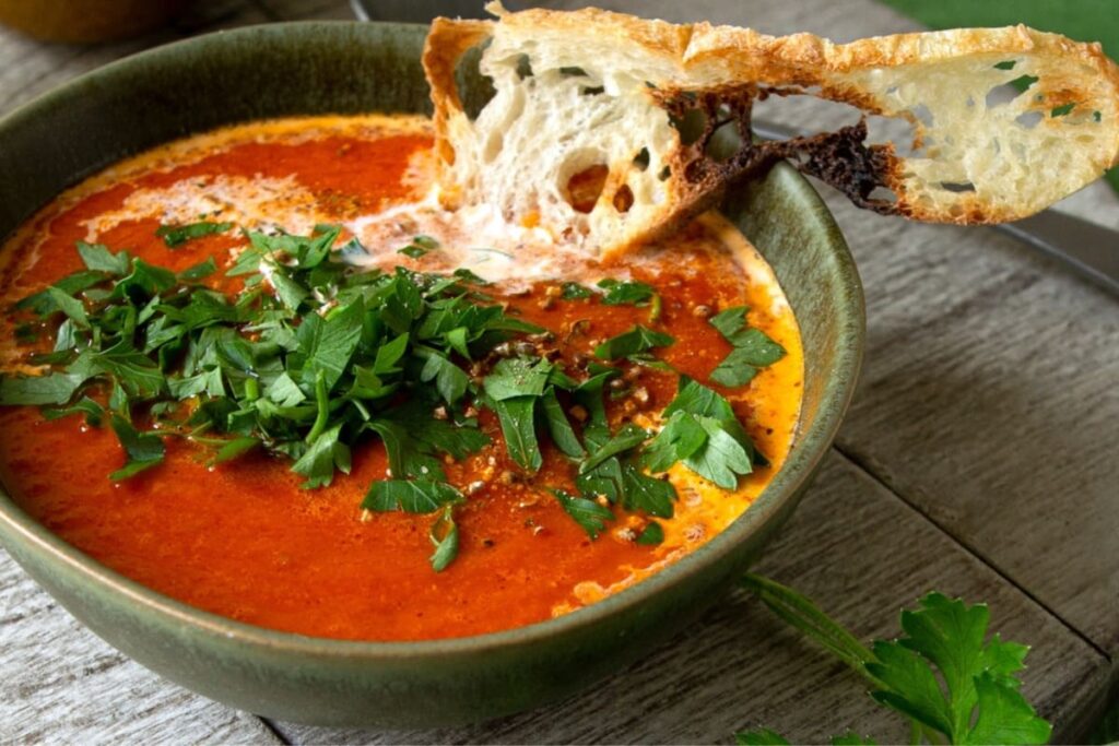 Supa crema de ardei copti cu smantana, decorata cu patrunjel si servita cu o felie de paine