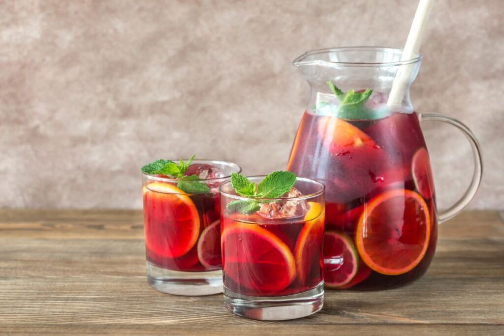 Carafa si pahare cu sangria decorate cu menta pe masa din lemn