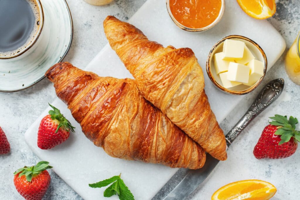 Croissante cu unt alaturi de gem, unt, cafea si fructe