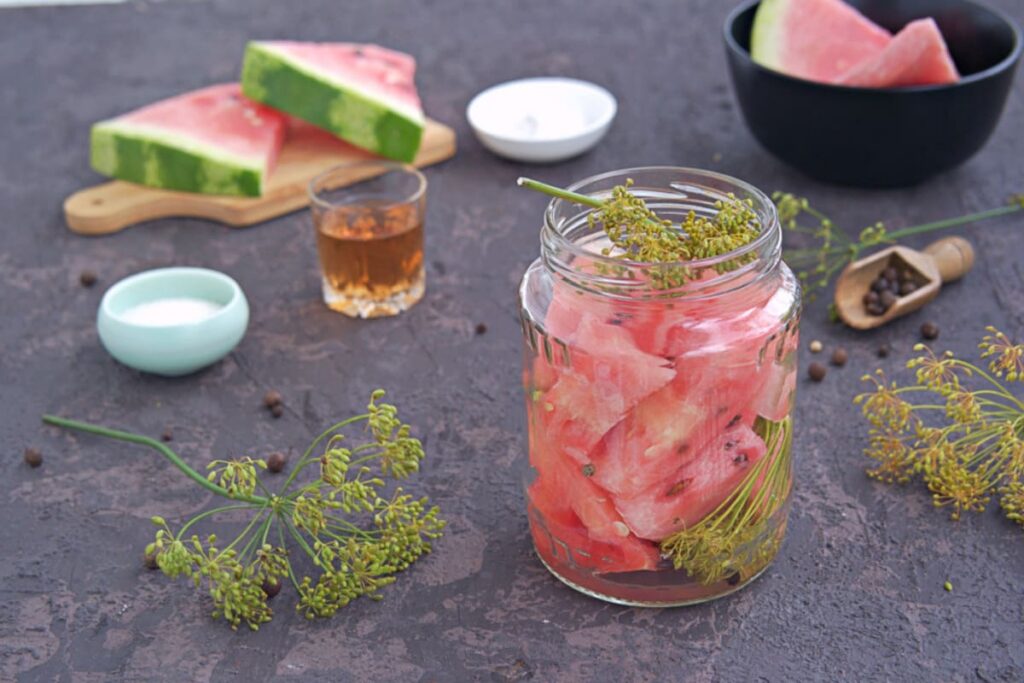 borcan cu pepene pus pentru murat, tije de marar si condimente pe masa